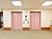 クリーム色の壁にピンク色のエレベーターが2台並んでいる。真ん中にボタンがあり頭上には時計もかかっている。