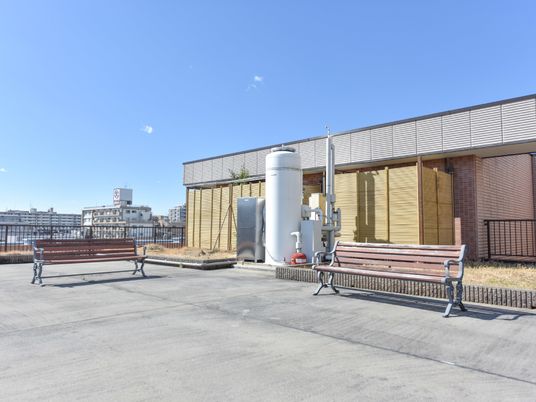 施設の写真 屋上からは街を見下ろすことができる。コンクリートの地面の上にタンクや長い木製のベンチが2台並んでいる。