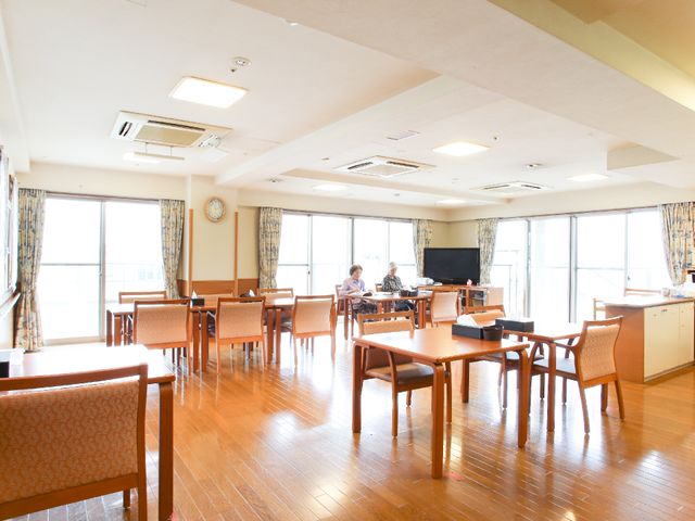 広々としたダイニングルーム 共用スペース 太陽の光が差し込むダイニングルームで、利用者同士がリラックスした空気の中、会話を楽しんでいます。フロアは清潔感にあふれ、居心地のよさを感じさせます。