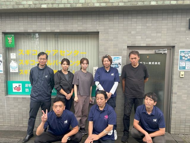 看板前のスタッフ 外観 施設前に集まったスタッフの皆さんです。チームワークを大切にする職場の雰囲気が伝わります。