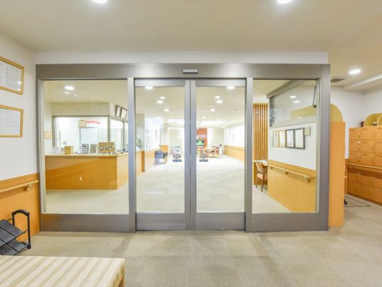 シルバーの枠に大きな透明ガラスがはめ込まれたデザインの自動ドアが設置されている。床にはグレーの絨毯が敷いてある。