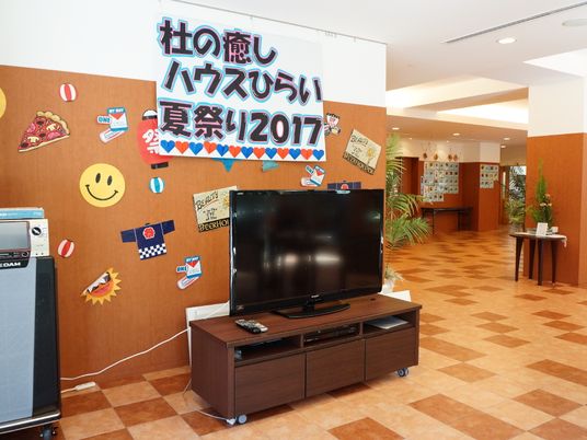スペースの隅に大型テレビが置かれている。カラオケシステムも完備している。壁には夏祭りの飾りが貼られている。
