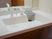 サムネイル 白色の洗面台スペースである。正面は鏡で、洗面の両側は、小物などが置けるスペースがある。蛇口レバーの横には石鹸置きがある。