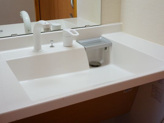 白色の洗面台スペースである。正面は鏡で、洗面の両側は、小物などが置けるスペースがある。蛇口レバーの横には石鹸置きがある。