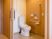 サムネイル 施設の写真 エル字型の手すりやオレンジの呼び出しボタン、操作パネルが壁に付いているふたのない便座が設置されたトイレ。