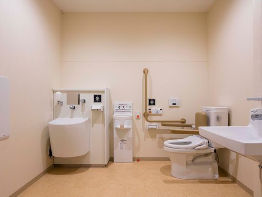施設の写真 広いトイレには背もたれや手すりが付いたトイレやベビーチェア、オレンジの呼び出しボタンなどがある。