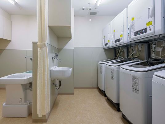 施設の写真 縦型の洗濯機が４台あり、それぞれの洗濯機の上に乾燥機も設置されている。
