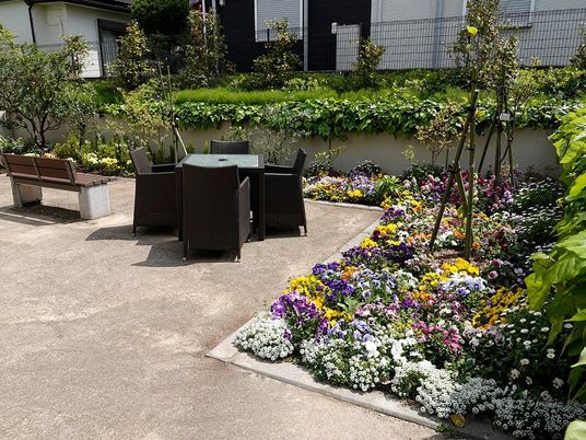 施設の写真 たくさんの花が咲く花壇があるスペースにはベンチやテーブルセットが置かれている。