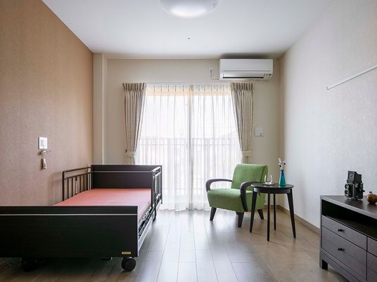 施設の写真 介護ベッドやエアコンが付いたフローリングの部屋。ベッドサイドには緊急通報装置もある。