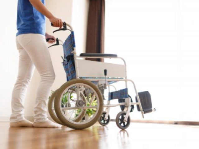 車椅子を押す人の足元 スタッフが車椅子をスムーズに押しています。廊下はゆったりとしており、作業が行いやすい環境が整っています。