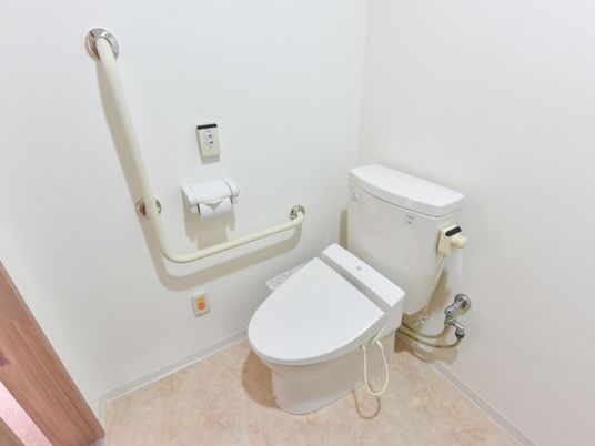 白を基調とした明るく、清潔感のあるトイレ。手すり、緊急通報装置が設置されている。車椅子での利用もストレスのない広々としてスペース。