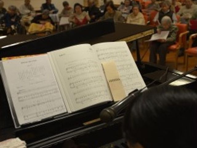 ピアノ演奏と集う人々 レクリエーション 明るく開放感のある空間で、ピアノの生演奏を楽しむ様子です。居心地が良く、音楽で心豊かな時間を過ごせる場所になっています。