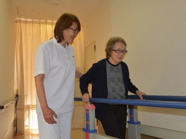 歩行訓練する利用者とスタッフ リハビリ 笑顔のスタッフが優しく支えながら、歩行訓練に励む様子が伝わってきます。安心してご利用いただける環境が整っております。