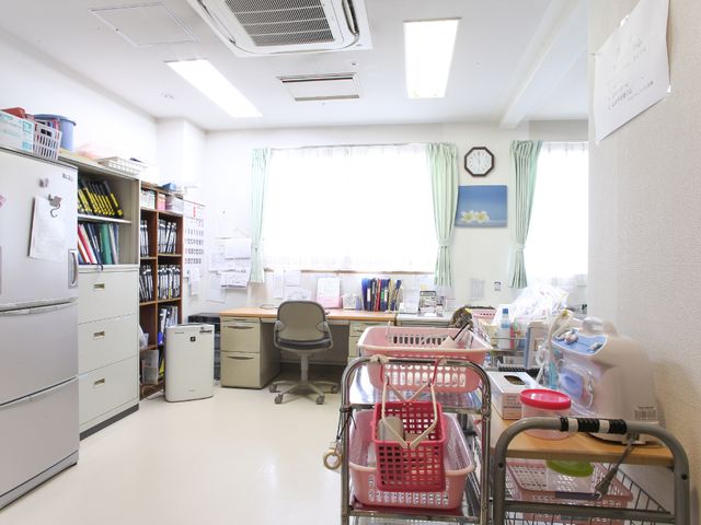 スタッフルームの様子 事務所 整然と配された資料や備品は、日々の業務がしっかりと行われていることを示しています。窓から自然光が差し込む明るいワークスペースが確保されています。