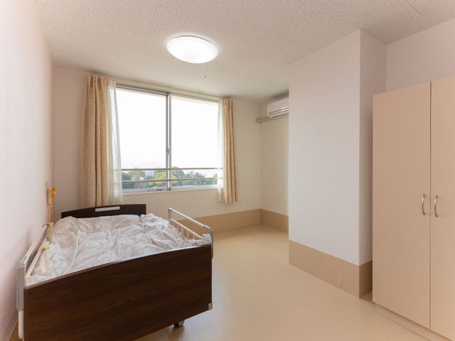 居室の窓辺とベッド 居室 日差しが入る明るい個室で、快適にお過ごしいただけます。壁面の収納には個人の荷物を整理して保管できます。