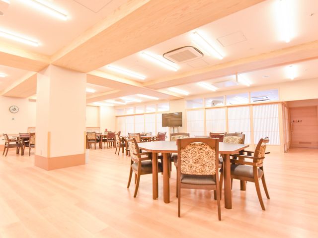 広々とした明るい食堂 談話室 広々とした空間で木目と和風のスクリーンが調和した食堂です。ゆったりした時間を過ごせる場所を提供しています。