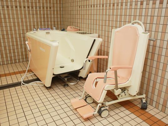 広い浴室に、車椅子タイプの入浴装置が置かれている。ピンク色と白で統一された空間で、居心地の良い入浴スペースになっている。