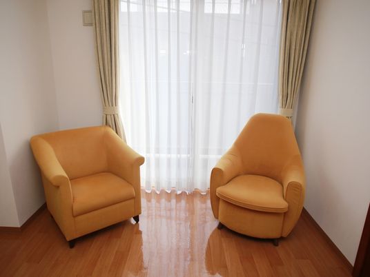 掃き出しの窓のそばにオレンジ色の一人掛けソファが２脚置かれている。艶のあるフローリングとソファの色からあたたかみを感じられる。