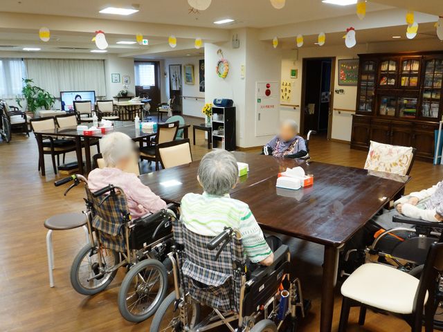 座っている人が多いリビング 共有スぺ―ス 椅子に座る住人たちがくつろぐ、明るく広々とした空間です。お互いのコミュニケーションも活発に見えます。