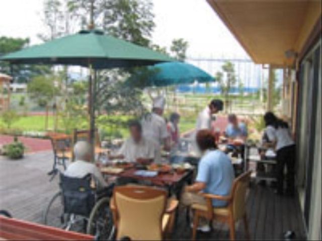 屋外テラスで食事をする人々 レクリエーション 開放感あるテラスで、利用者が心地よいひとときを過ごしている様子です。職員も一緒になって、穏やかな時間が流れています。