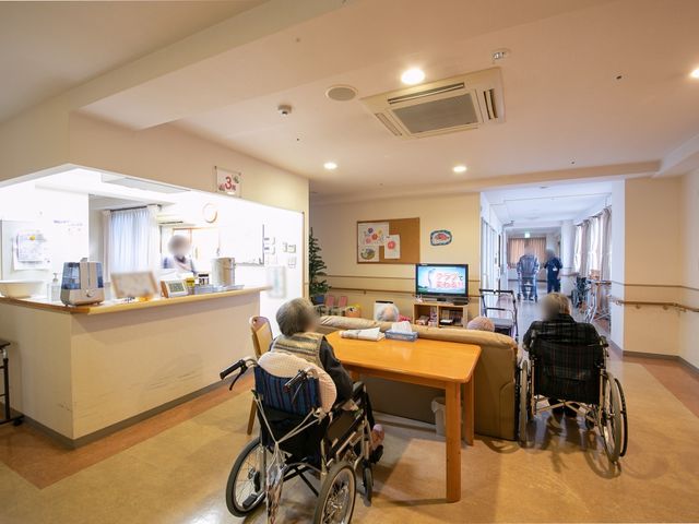 共用ラウンジの日常風景 共有スペース ゆったりとしたラウンジでは、入居者がテレビを観ながらくつろいでいます。働くスタッフの温かな配慮が感じられる空間です。