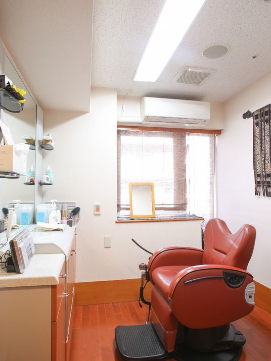 施設内で散髪する部屋。専用の椅子が一台、その向かい側に鏡、また脇には散髪に必要な用具が置いてある。エアコンと窓がある。