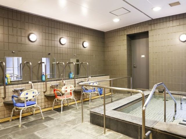 清潔感のある明るい浴室 大浴場１ 広々としたバリアフリー設計の浴室です。利用者の安全と快適さを考えた椅子や手すりが整っており、日々の暮らしをサポートします。