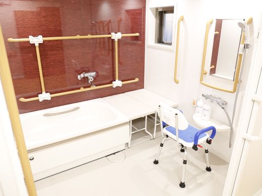 浴槽の壁には縦と横に2本の手すりが付いており、横には台が設置されている。介護用のシャワー椅子も置かれている。
