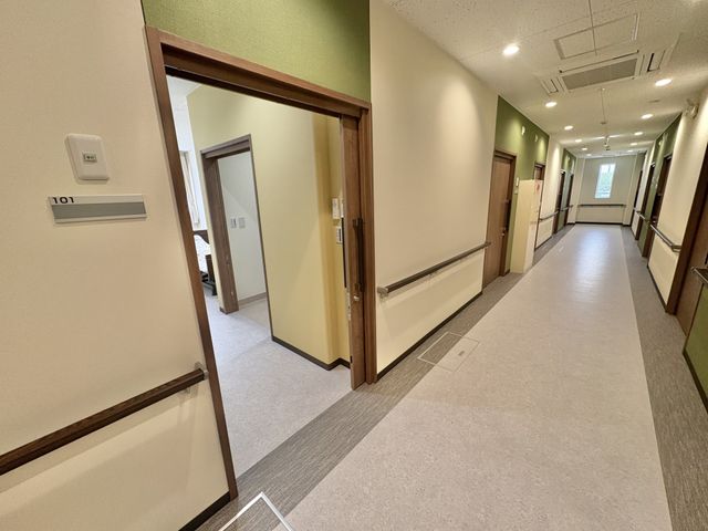 廊下の居室前 廊下   手すりが続く明るい廊下で、居室の出入りがしやすい造りです。扉が並び、静かに移動できる落ち着いた雰囲気です。