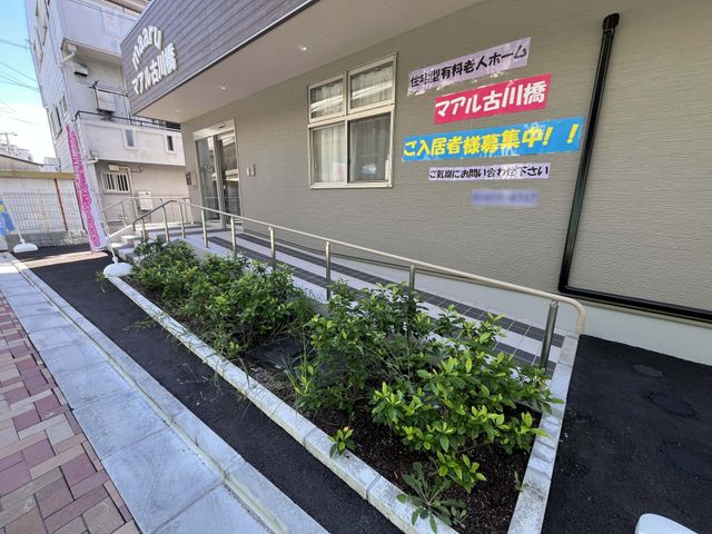 建物外観と看板の入口 外観   スロープ付きの入口で、手すりが設けられています。募集案内の看板があり、就業先の雰囲気を外から確認できます。