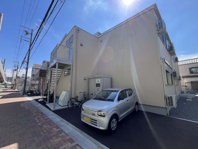建物外観 外観   青空の下に建つすっきりした外観で、駐車スペースや自転車置き場が見えます。就業時の出入りや送迎の動線をイメージしやすいです。
