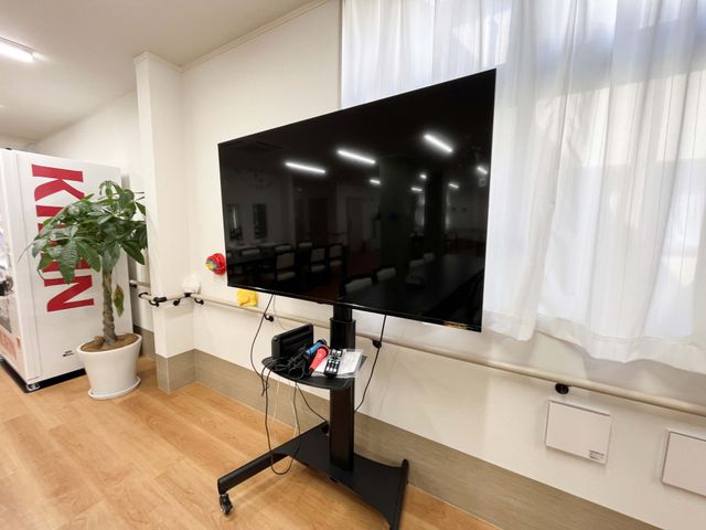 テレビのある共有スペース リビング   大きなテレビが配置された明るい共有スペースです。窓際のやわらかな光が入り、くつろぎや交流の場として使いやすそうです。