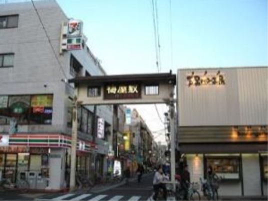 鳥居のような形の大きな門があり、上部に商店街の名前の入った大きな木製の看板が掲げられている。その門の左にはコンビニがある。