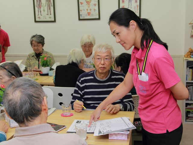 機能訓練の風景 明るい色調の部屋で、利用者が機能訓練に取り組んでいます。スタッフが丁寧にサポートしており、やりがいある職場です。