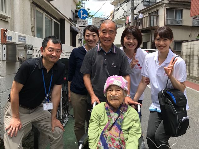 笑顔のスタッフと利用者 陽気なスタッフが車椅子の方を囲んで笑顔で立っており、働く環境の温かさが感じられます。チームワークの良さが伝わる一瞬です。