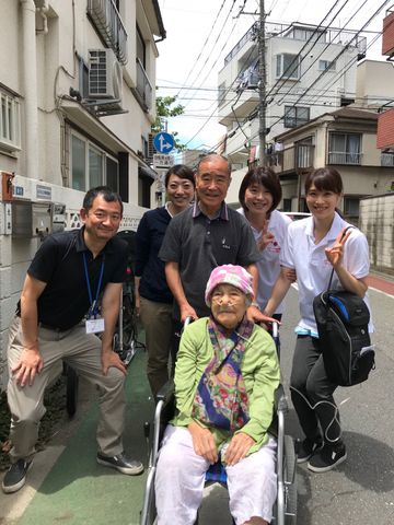 笑顔のスタッフと利用者 陽気なスタッフが車椅子の方を囲んで笑顔で立っており、働く環境の温かさが感じられます。チームワークの良さが伝わる一瞬です。