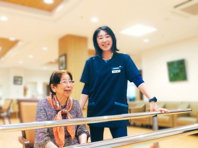 明るい室内の様子 機能訓練室 笑顔のスタッフが、利用者と一緒にリハビリのサポートをしています。広々とした快適な空間です。