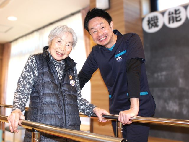 笑顔のスタッフと利用者の機能訓練室 機能訓練室 明るく親しみやすい空間では、利用者様が安心してリハビリに励めます。スタッフのサポートも万全です。