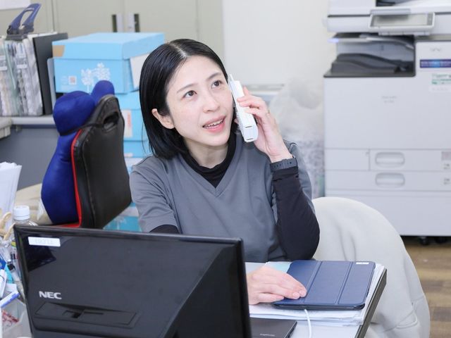 オフィスの一角 スタッフイメージ スタッフがデスクで作業する様子です。電話対応をしながら、書類を扱っているようです。