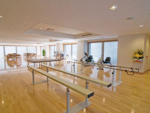 広々とした施設の室内 機能訓練室 自然光が降り注ぐ明るいスペースで、リハビリ機器が整っています。快適な環境で運動可能です。