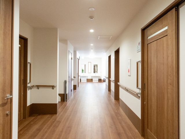 木目の廊下 廊下 木目調の広々とした通路で、移動がスムーズです。壁には手すりがあり、安全性が考慮されています。