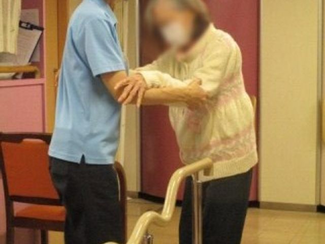 支援中の介護士と利用者 内観 介護士が優しくサポートし、明るい室内で利用者がリハビリに取り組んでいます。