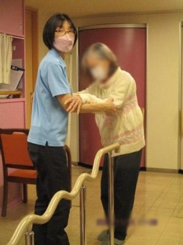 支援中の介護士と利用者 内観 介護士が優しくサポートし、明るい室内で利用者がリハビリに取り組んでいます。