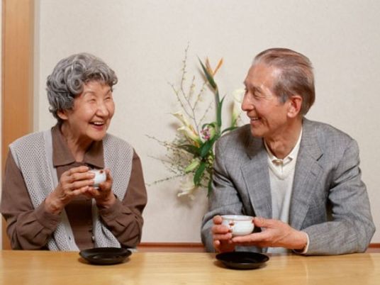 男性と女性の入居者様がテーブル向かって座り、お茶を飲んでいる場面である。二人とも笑顔で、楽しそうに会話をしている。