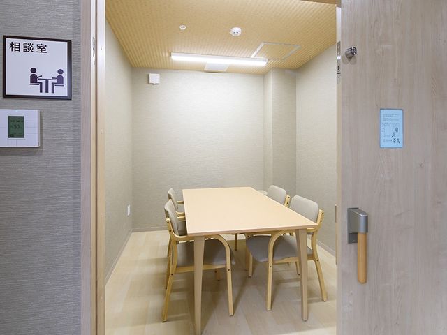 相談室の小さな会議机 多目的室   落ち着いた相談スペースで、少人数で話しやすい机配置です。入口が広く、来訪者対応や面談の場として使いやすそうです。