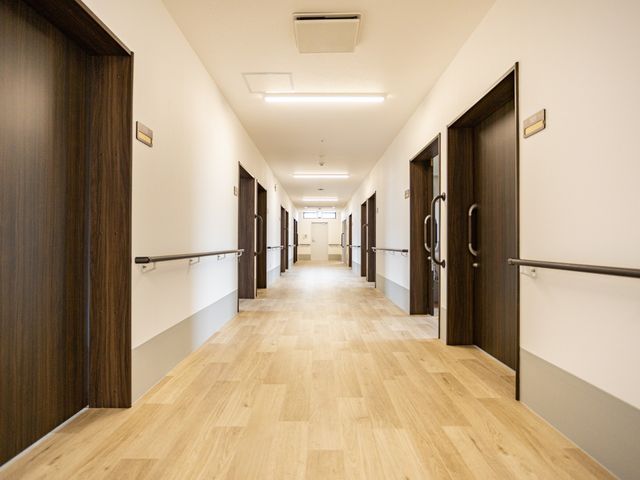 手すり付きの明るい廊下 廊下   木目の床と白い壁で、明るく見通しのよい廊下です。両側に居室の出入口と手すりがあり、移動しやすい印象です。