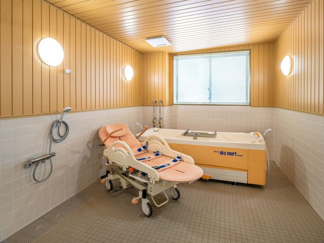 機能訓練室の浴槽 浴室   明るい浴室に、移乗しやすい介護用の浴槽が設置されています。手すりやシャワーも見え、入浴介助のしやすさがうかがえます。