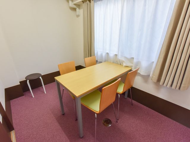 明るい居室のテーブルと椅子 相談室 居室には清潔感のあるテーブルが置かれ、日差しが柔らかに差し込む心地よい空間です。ゆったりと過ごす時間を大切にしています。