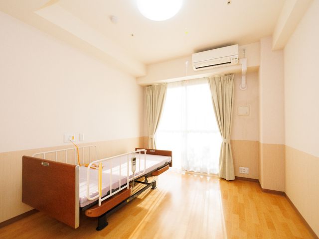 明るい個室のベッド 居室 木目調のフロアが温かみを感じさせる個室です。開放感のある窓が明るい日差しを取り込んでいます。