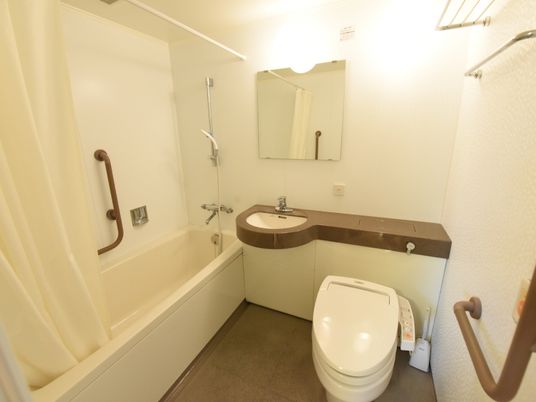 白基調の内装。便器の前方壁面と、浴槽内壁面に手すりが設置されている。トイレ付近には非常用ボタンがある。